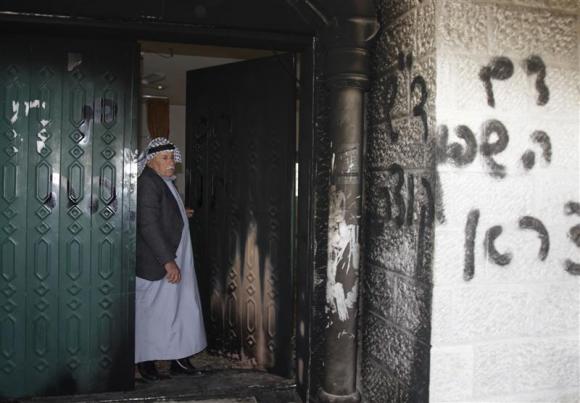 A Palestinian man stands near a door and wall of a mosque which were vandalised in the West Bank village of Deir Istiya